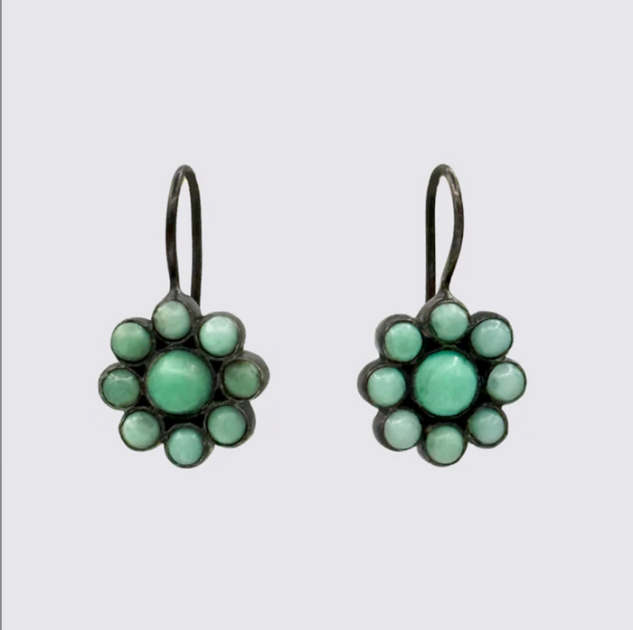 Pair of flower-shaped earrings with green gemstones on a light gray background