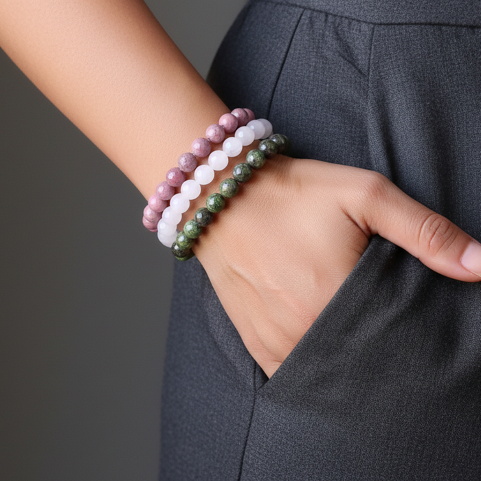 Close-up of a person wearing three beaded bracelets on a plain background