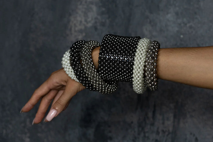 six kind of handcrafted modular bracelet cuff from syntethic japanese pearl and metal beads on wrist of woman in grey background