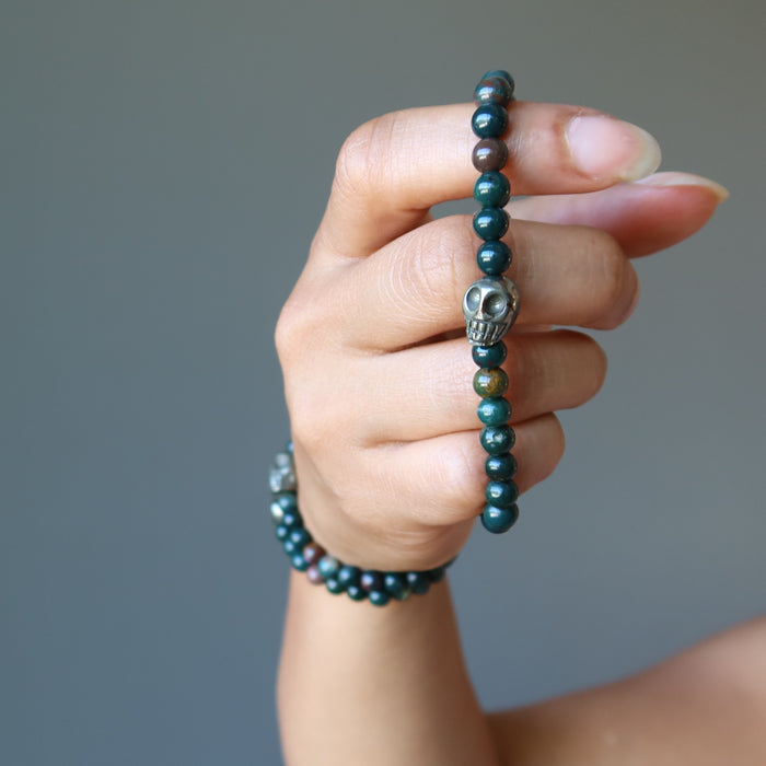 hand wearing and holding pyrite skull and round bloodstone beaded stretch bracelets
