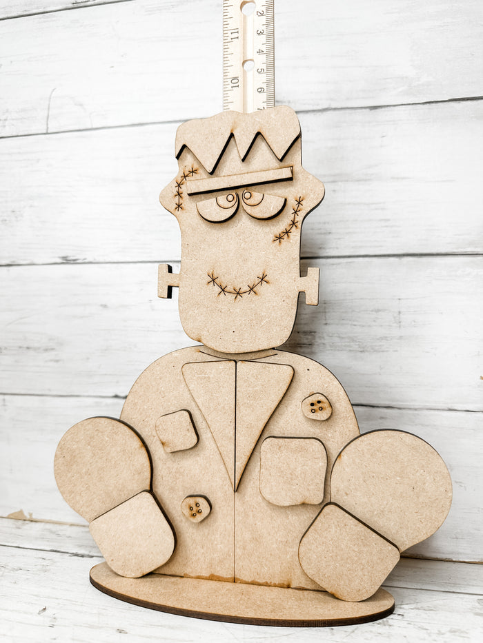 Unpainted Frankenstein monster shelf sitter assembled with layered hair, face, jacket, patches, shoes, and stand