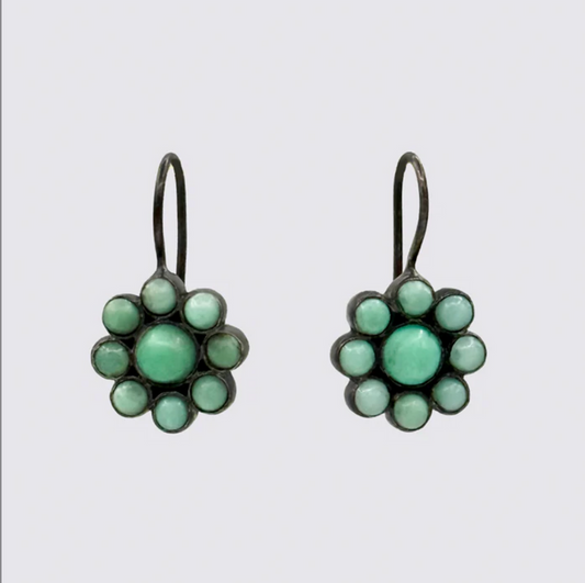 Pair of flower-shaped earrings with green gemstones on a light gray background