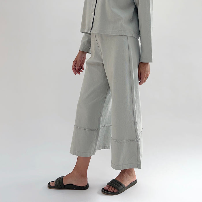 Three-quarter front view of model wearing Pacific Cotton orlaya crop full pant, showing elastic waistband, wide flared leg silhouette, layered hem panel, and cropped length