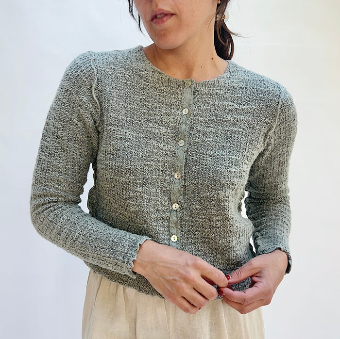 Person wearing a textured gray cardigan against a white background