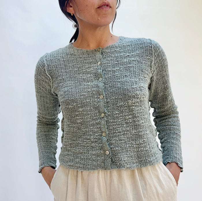 Person wearing a textured gray cardigan against a white background