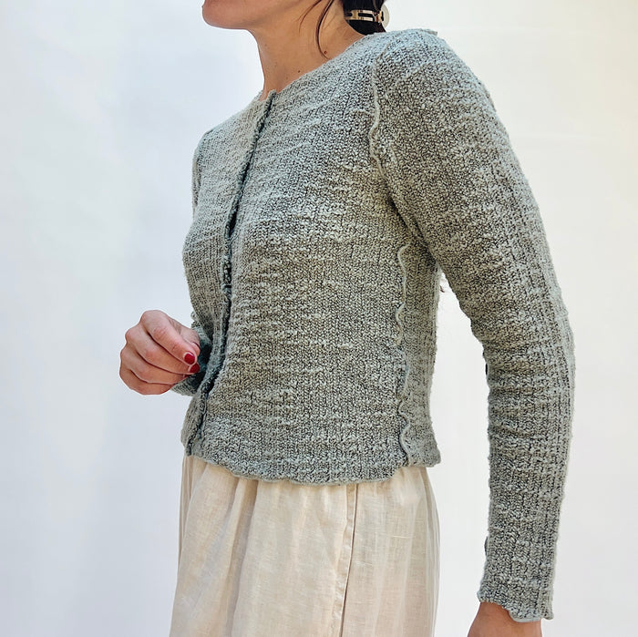 Person wearing a textured gray cardigan against a white background, viewed from the side
