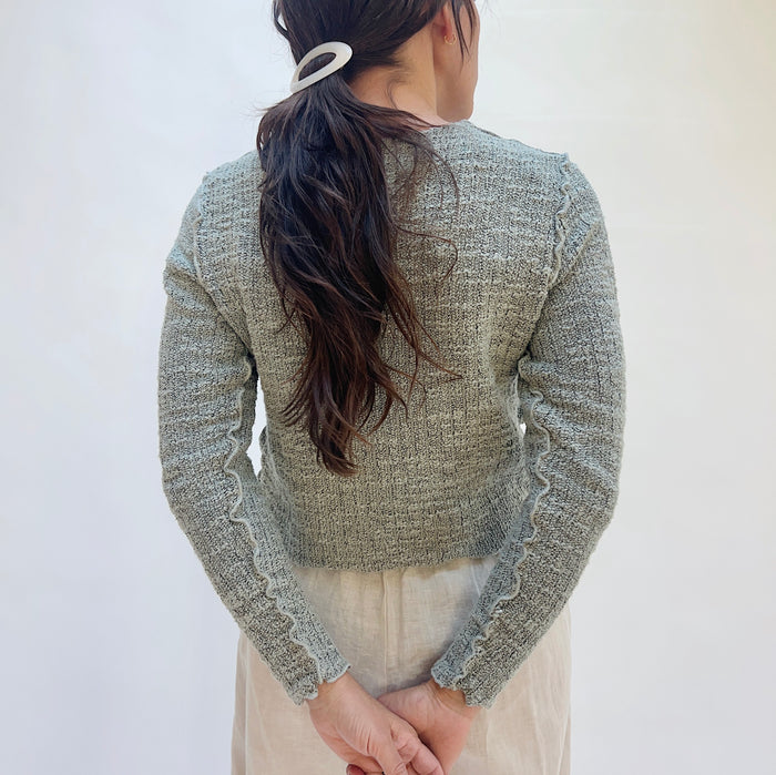 Person wearing a textured gray sweater against a white background, viewed from the back