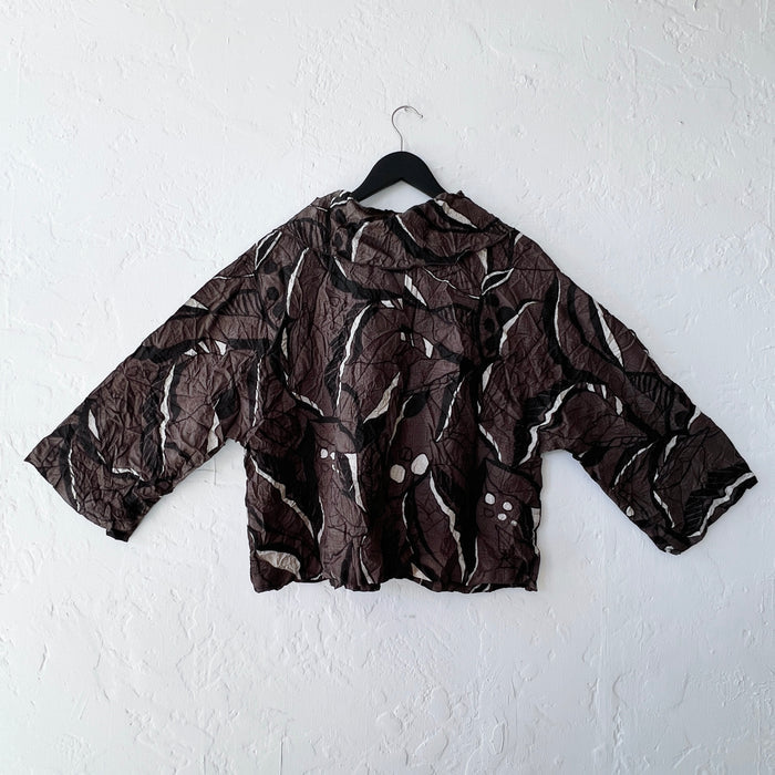 Brown leaf patterned shirt on a hanger against a white wall