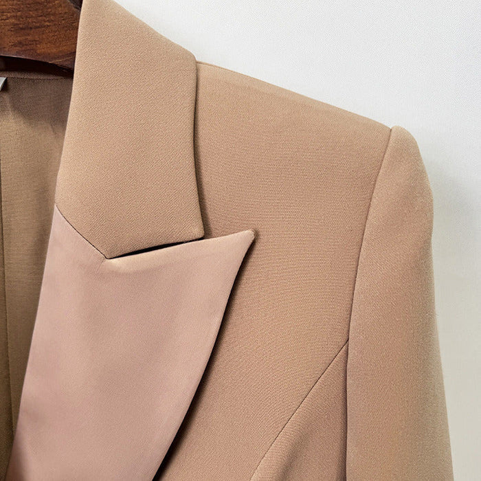 Close-up of a beige tailored blazer with structured shoulders and a satin-like lapel, shown hanging against a plain light background.