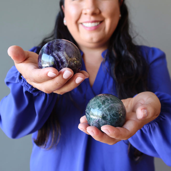 model holding green purple rainbow Fluorite Spheres one on each hand