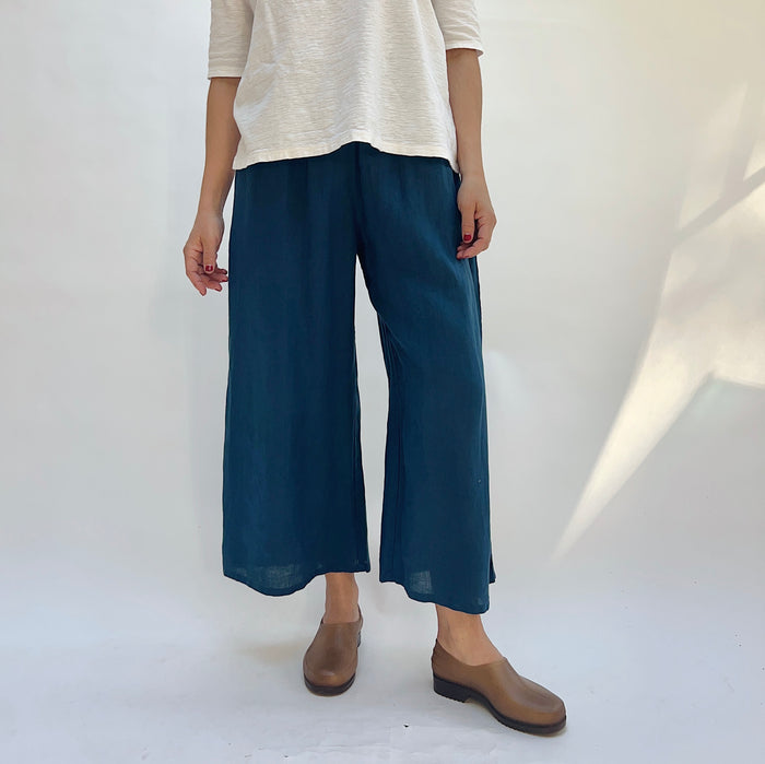 Person wearing a beige top and blue wide-leg pants on a white background
