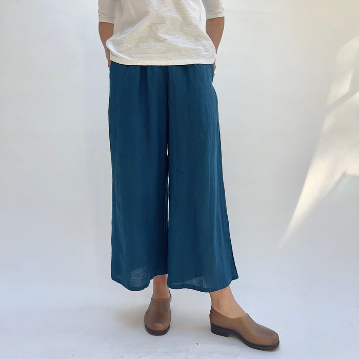 Person wearing blue wide-leg pants and a white shirt on a plain background