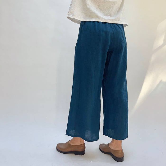 Person wearing blue wide-leg pants and brown shoes on a white background, viewed from the back