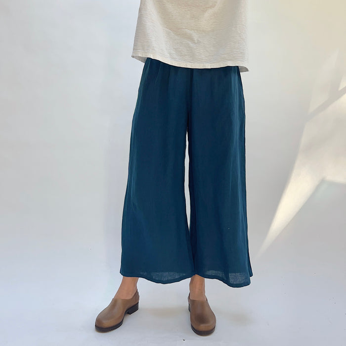 Person wearing blue wide-leg pants and brown shoes on a white background