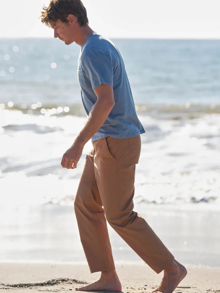 Man walking on a beach wearing a blue shirt and beige pants.