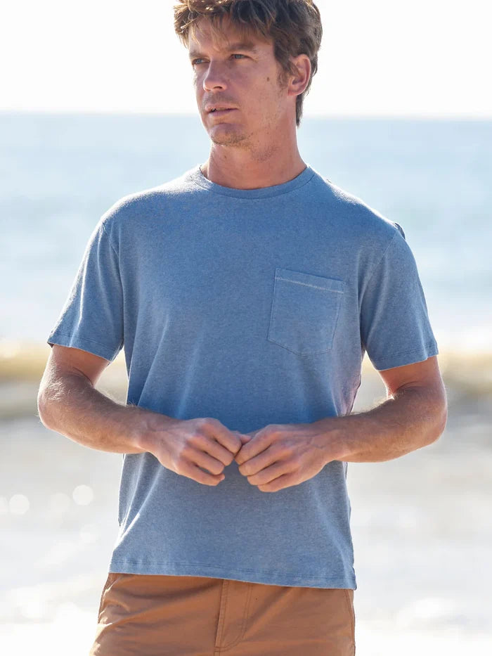 Man wearing a blue t-shirt with a pocket, standing against a blurred natural background