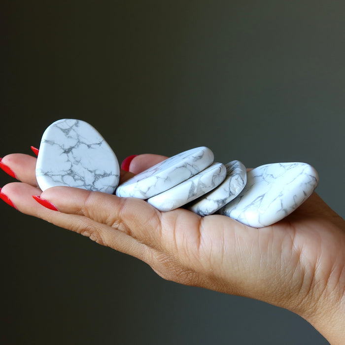 Hand holding five white howlite stones against a dark background