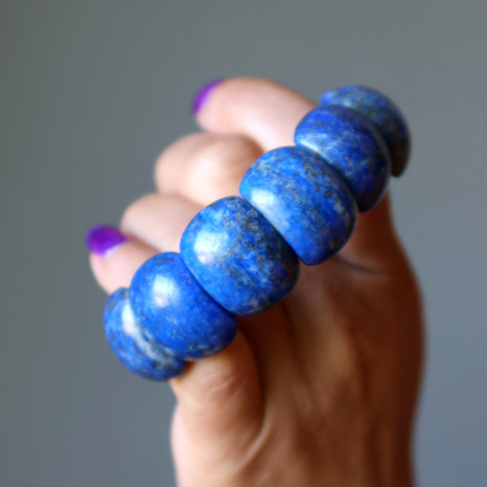 Hand holding a blue Lapis bracelet against a gray background