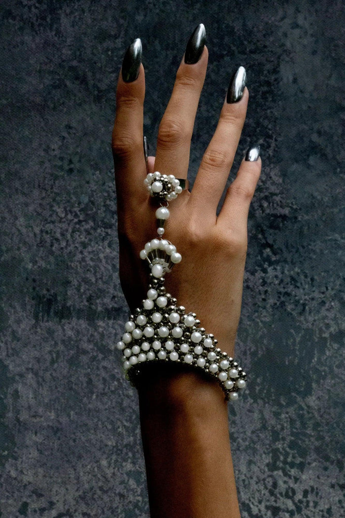 Hand wearing a decorative pearl bracelet and ring against a dark textured background
