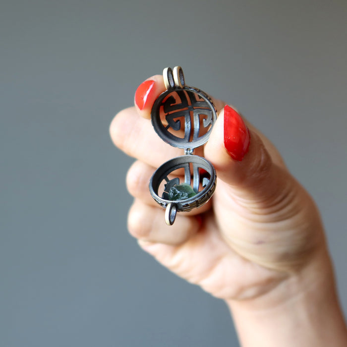 hand holding an open locket with green moldavite gemstone