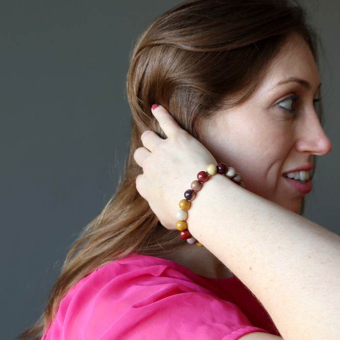 holly of satin crystals with hand in hair wearing multi colored mookaite jasper round beaded stretch bracelet