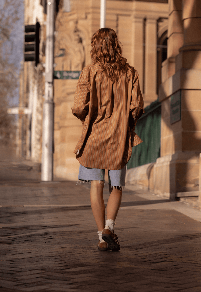 Back view of a model walking in caramel stripe organic cotton oversized shirt, dropped shoulder, long sleeves