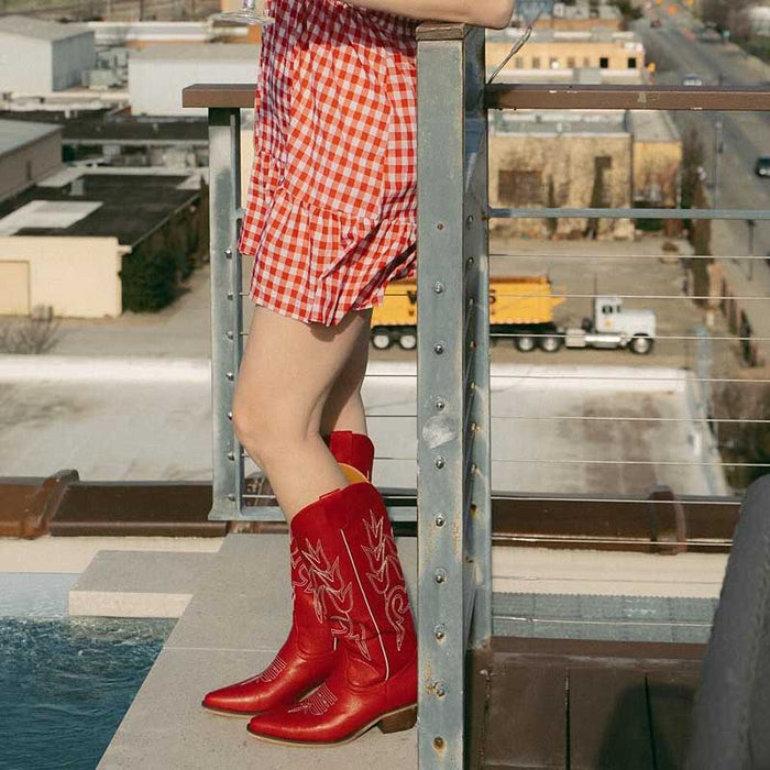 Stylish red chunky cowgirl boots for women paired with a gingham dress on a rooftop setting