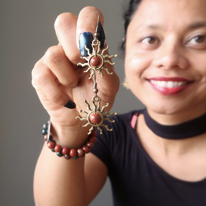 woman holding red jasper stone earrings with sun-shaped designs