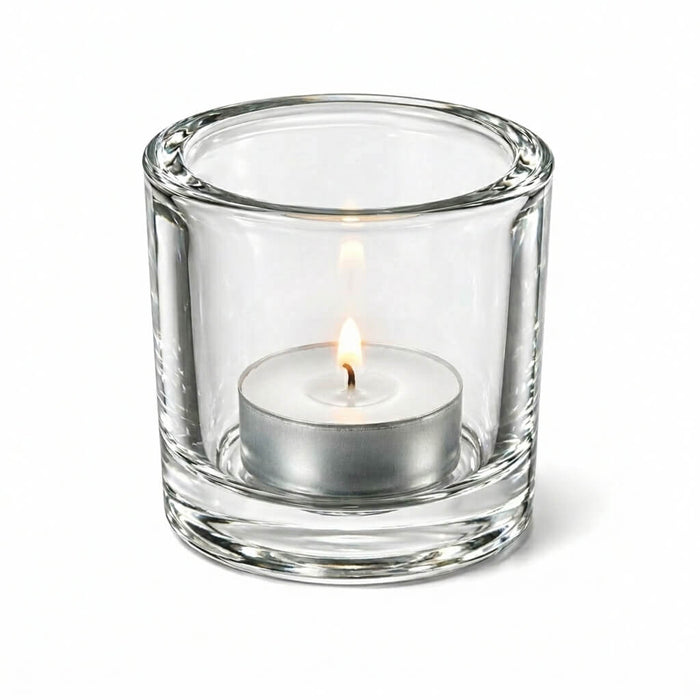 Lit tealight candle in clear glass holder on white background