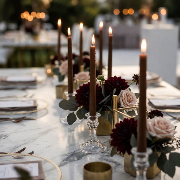 Outdoor dining table with lit brown taper candles and romantic floral arrangements