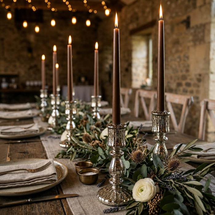 Lit brown taper candles on a long rustic dining table with floral decor