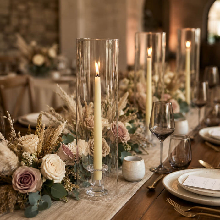 Lit ivory taper candles in glass hurricanes on rustic dining table