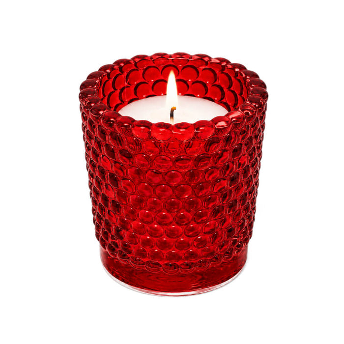 Red hobnail glass votive holder with glowing candle on white backdrop