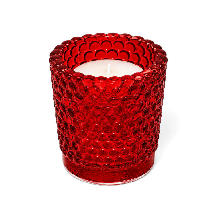 Red hobnail glass votive holder with white candle on white background