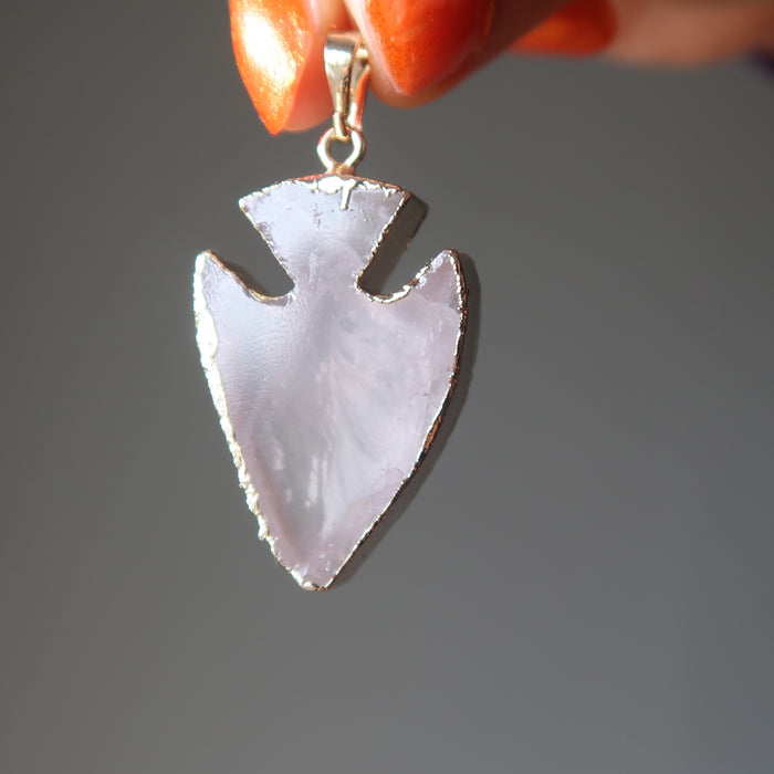 hand holding a rose quartz arrowhead pendant