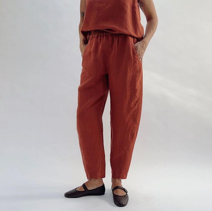Front view of the Seamed Taper Pant in Terracotta by Yuvita, showing the elastic waistband, side pockets, and tapered ankle, styled with a matching terracotta linen tank and dark Mary Jane flats