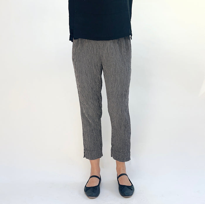 Person wearing black and gray checkered pants and black shoes on a white background