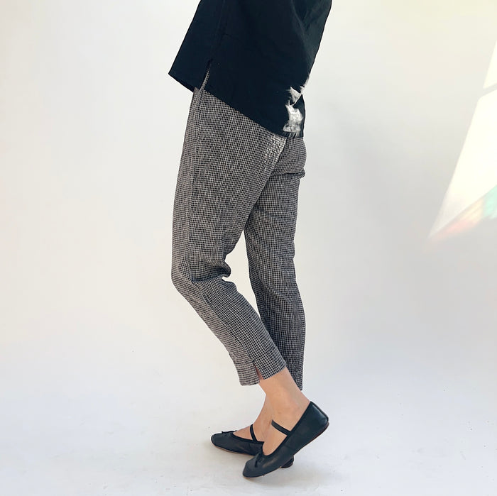 Person wearing gray and black checkered pants and black shoes on a white background, viewed from the side