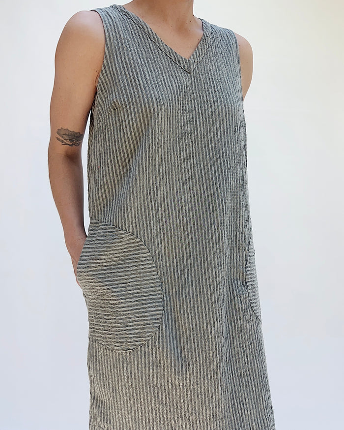 Person wearing a sleeveless, striped dress with a pocket on a plain background