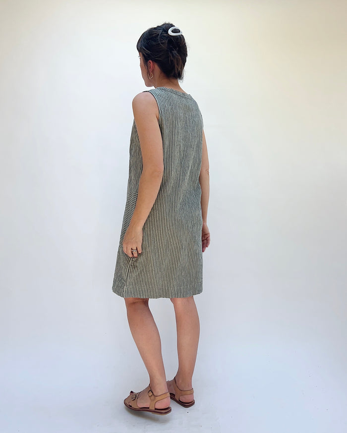 Person wearing a green striped dress against a white background, viewed from the back