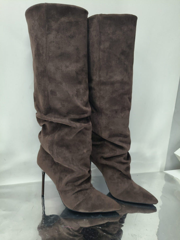 A pair of tall brown suede knee-high boots with pointed toes and slim high heels, standing on a reflective surface against a light gray background.